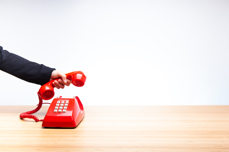 Business woman hanging up old red telephone, classic red telephone receiver in hand wearing black suit, old telephone isolated on white background and wooden desktop.の写真素材
