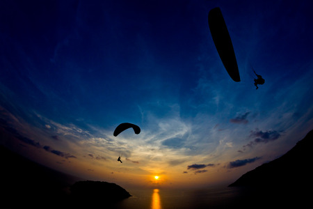 Paraglide silhouettes flying above the sea against colorful sunset background. Promthep Cape, Phuket, Thailand.の写真素材