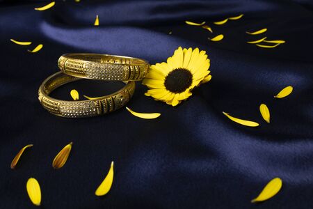 Gold Plated bangles on dark blue background with yellow flowerの写真素材