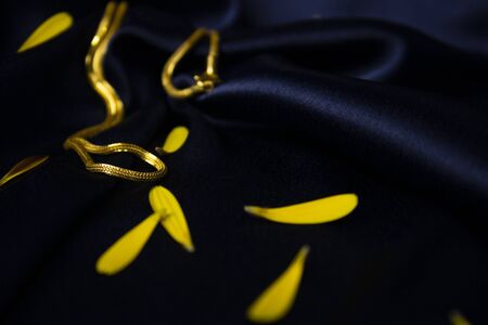 Gold Chain on blue silky background with yellow flower palletsの写真素材