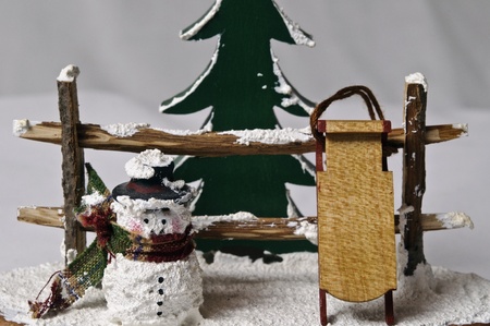 snowman with sleigh in front of rail fence and pine tree