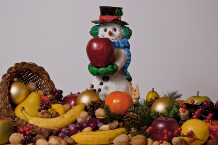 snowman figurine holding apple surrounded by a cornucopia of fruits and nutsの写真素材