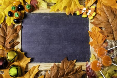 Blank chalkboard on burlap framed with autumn leaves small bells and halloween candy with copy space...