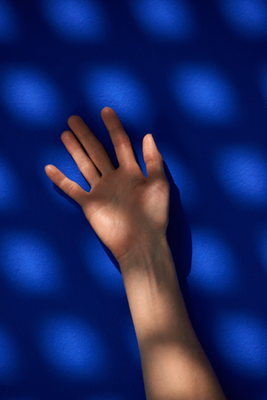 The woman hand in sun-dappled on the background of blue wallの写真素材