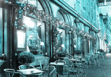 Cafe decorated for Christmas holidays. In foreground are tables and chairs for the clients standing on the street. Holiday toned background.の写真素材