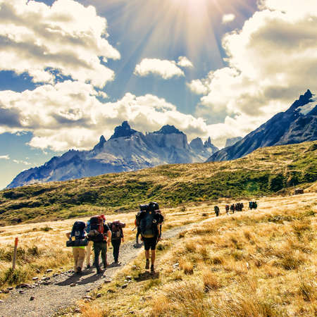 Group of travelers with backpacks walk along a trail towards a mountain ridge by sunny day. Backpackers and hikers style. Concept of active leisureの写真素材