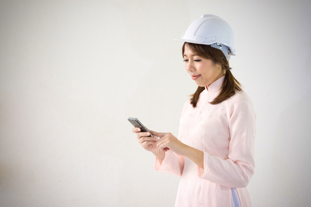 Young vietnamese woman with safety helmet holding smartphone.の写真素材