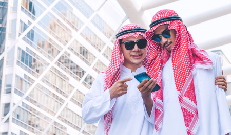 Two Arab businessmen messaging on a mobile phone in cityの写真素材
