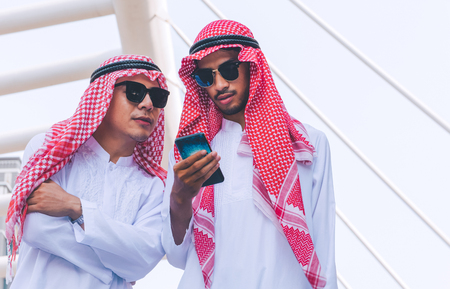 Two Arab businessmen messaging on a mobile phone in cityの写真素材