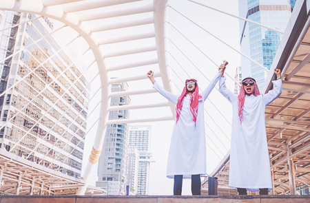 Two Arab businessmen standing by raising both hands up in cityの写真素材