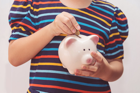 Cute little girl putting coin into piggy bankの写真素材