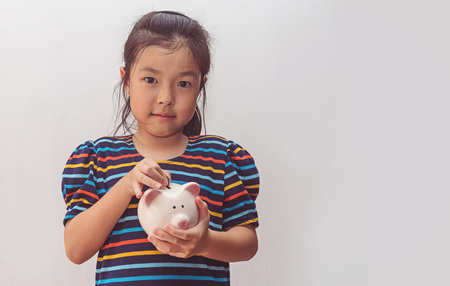 Cute little girl putting coin into piggy bankの写真素材