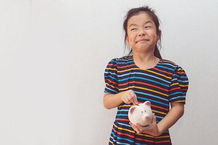 Cute little girl putting coin into piggy bankの写真素材