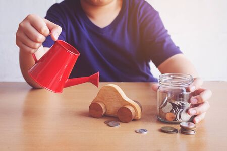 Boy watering car and coins. plan for car conceptの写真素材