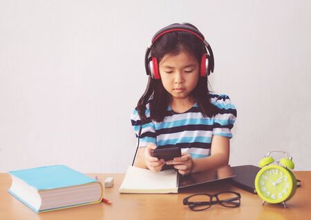 Asian little girl writeing a book and headphones listening to music.の写真素材