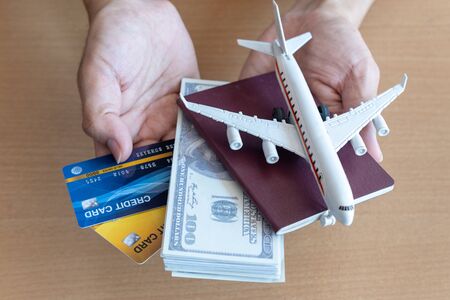 Man hands holding 100 dollar bills and airplane on wooden table. Travel concept