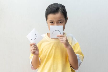 Girl holding paper happy and sad symbolizing changing emotionsの写真素材