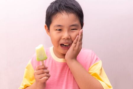 Asian boy with hypersensitive teeth eating eating a colorful frozen popsicle in the summerの写真素材