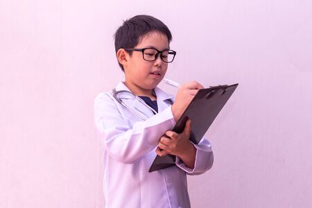 Asian boy playing doctor with stethoscope in hands and writing on clipboardの写真素材