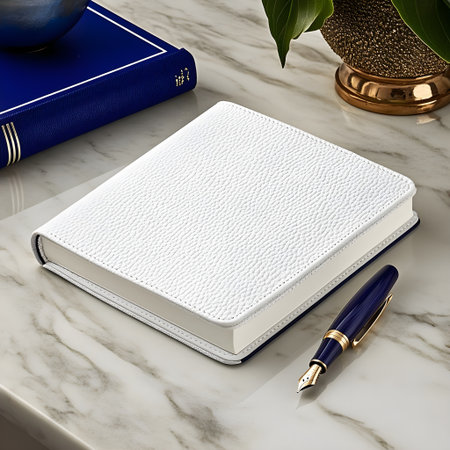 A white leather bound notebook with textured cover sits elegantly on marble surface, accompanied by blue and gold fountain pen. blue book and potted plant add sophistication to sceneの素材