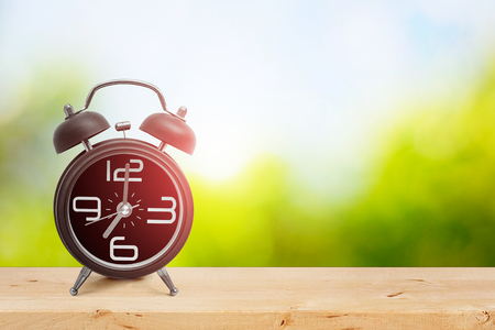 Vintage alarm clock showing seven o'clock on wooden table with natural green and blue sky background.の写真素材
