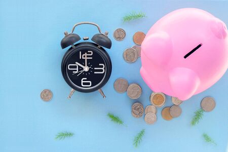 Top view of black alarm clock with pink piggy bank and coins on blue background-Saving conceptの写真素材