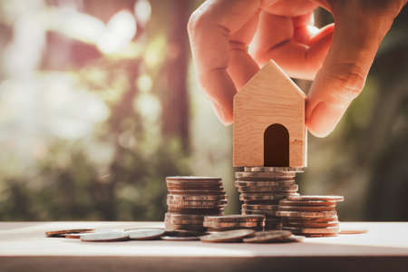 Hand holding house model put on stack coins