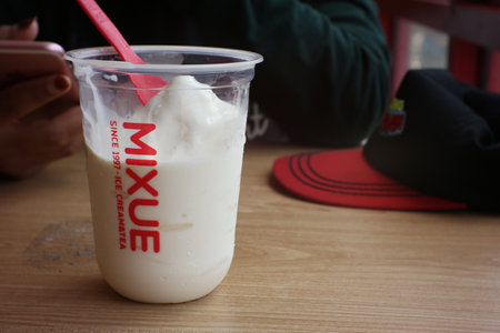 ice cream in plastic cup with red straw on the wooden table.