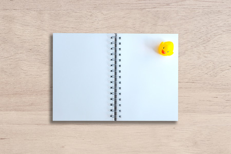 white page of notebook and yellow duck on wood textureの写真素材