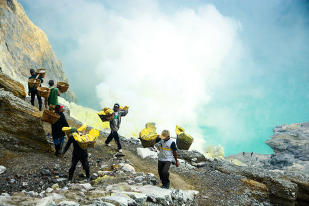 KAWAH IJEN INDONESIA  JANUARY 22 2013 : Miners carry baskets with sulphur in fumes of toxic volcanic gas from the sulphur mines in the crater of the active volcano of Kawah Ijen East Java Indonesia.のeditorial素材