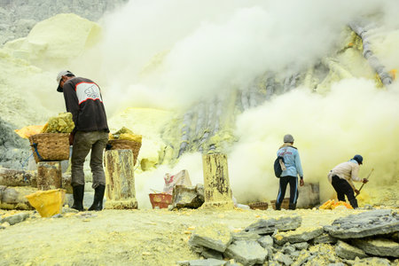 KAWAH IJEN INDONESIA  JANUARY 22 2013 : Miners carry baskets with sulfur sulphur in fumes of toxic volcanic gas from the sulfur mines in the crater of the active volcano of Kawah Ijen East Java Indonesia.のeditorial素材