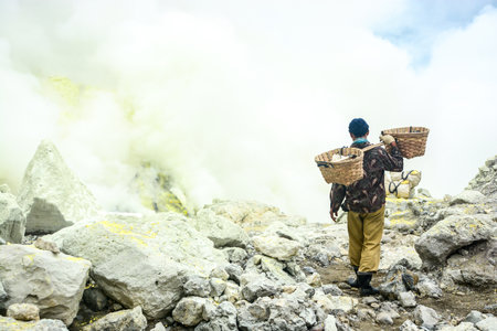 KAWAH IJEN, INDONESIA - JANUARY 22, 2013 : Miner carry baskets with sulfur sulphur from the sulfur mines in the crater of the active volcano of Kawah Ijen, East Java, Indonesia.のeditorial素材