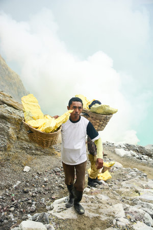 KAWAH IJEN, INDONESIA - JANUARY 22, 2013 : Miner carry baskets with sulfur sulphur from the sulfur mines in the crater of the active volcano of Kawah Ijen, East Java, Indonesia.のeditorial素材