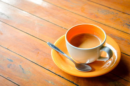 coffee in orange ceramic cup with spoon and saucer on grunge wooden tableの写真素材