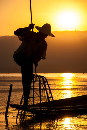 Silhouette Intha fisherman and traditional fishing net in beautiful sunset at Inle Lake, Shan state, Myanmarの写真素材