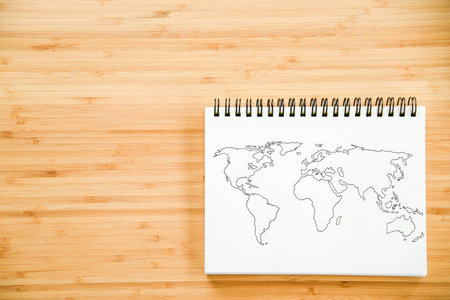 World map outline sketch on paper of binder notebook that placed on wooden floor background - can...