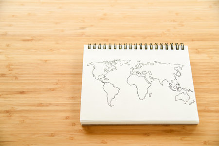 World map outline sketch on paper of binder notebook that placed on wooden floor background - can use for travel business or save the earth conceptsの写真素材