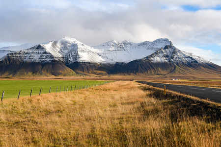 Empty road, yellow-green fields and snowcapped mountains, Beautiful landscape in early winter of Icelandの写真素材