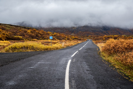 Empty road leading to mountain and majestic fog, Beautiful landscape in autumn of Icelandの写真素材