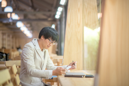 Young Asian casual business man using smartphone and checking his work at vintage cafe in the city, smart urban lifestyle with digital device and technology gadget trends, work life balance conceptsの写真素材
