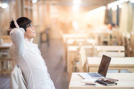 Young Asian happy man with headphones listening to music and working with modern laptop computer in vintage interior studio, gadget lifestyle and leisure activities conceptsの写真素材
