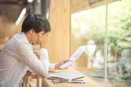 frustrated stressed business man checking chart and diagram report paper in workplace, young Asian entrepreneur fail in result and worried about deadline of job, risk management conceptsの写真素材