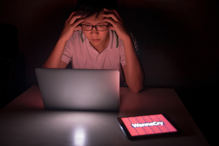 Young Asian male frustrated, confused and headache by WannaCry ransomware attack on desktop screen, notebook and smartphone, cyber attack internet security conceptの写真素材