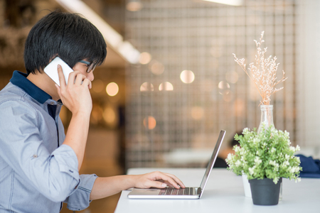 Young Asian man dressed in casual style working in coffee shop with his laptop computer and smart phone. Digital nomad and IT modern lifestyle, work life balance conceptの写真素材