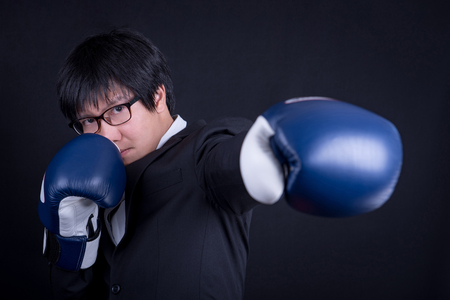 young asian business man wearing suit in boxing punching his left hand pose with black background studio. business man fight pose conceptの写真素材