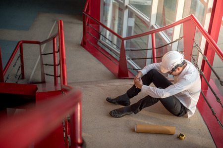 Engineer or Architect feeling tired and headache with his job. sitting on building stairs with architectural drawing on his side while wearing protective equipment safety helmet at construction siteの写真素材