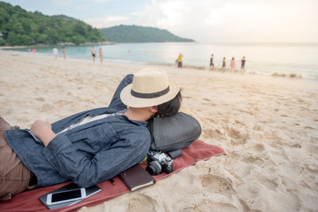 young Asian man lying on the beach and close his face by hat, vacation time and summer holiday conceptsの写真素材