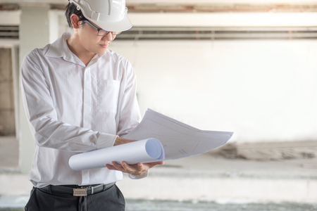 Engineer or Architect checking architectural drawing while wearing a personal protective equipment safety helmet at construction site. Engineering, Architecture and building construction conceptsの写真素材