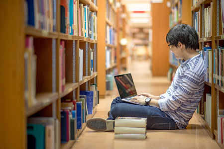 Young Asian man university student thinking about his project homework and using laptop computer in library, education research and self learning in university life conceptsの写真素材