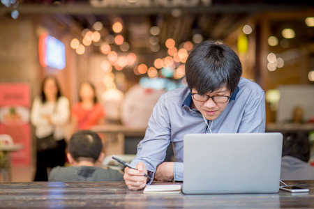 Young Asian Business man dressed in casual style contact with customer when working in cafe. Digital nomad lifestyle in public working space.の写真素材
